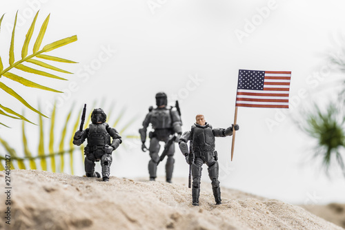 selective focus of toy soldiers holding american flag on sand hill