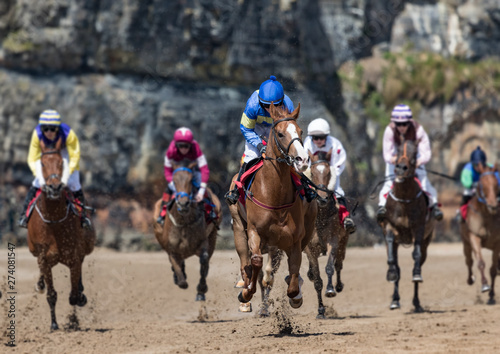 Head on view of galloping race horses and jockeys racing down the track, horse racing action on the beach, west coast of Ireland