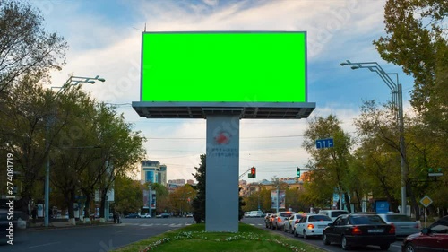 Wallpaper Mural 4K TIME LAPSE video. The Big Advertising billboard with green screen in the center of the autumn cityscape with traffic cars and people against the background of moving white clouds. Day becomes night Torontodigital.ca