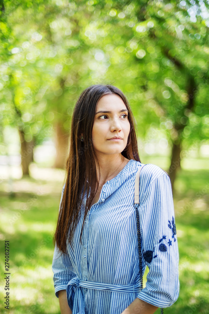 A girl of Asian appearance in a city park. Summer portrait of young Tatar on a background of green foliage