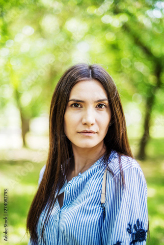 A girl of Asian appearance in a city park. Summer portrait of young Tatar on a background of green foliage