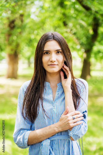 A girl of Asian appearance on a walk in a city park. Summer portrait of young Tatar on a background of green foliage