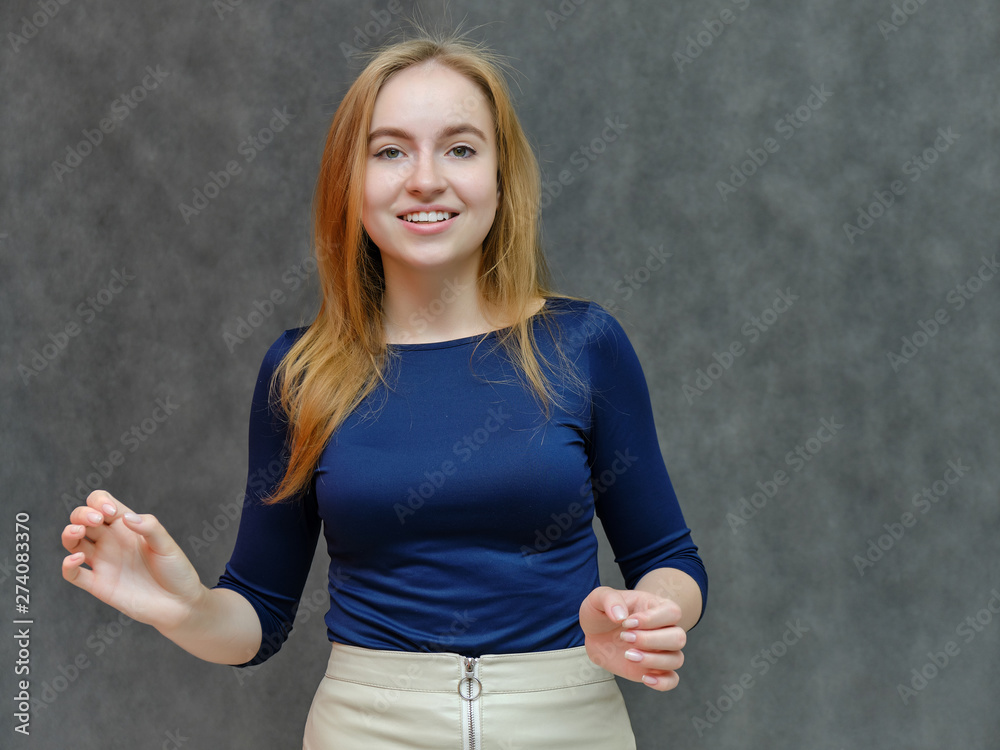 Concept portrait portrait of a beautiful smiling girl woman with red hair in a blue jacket. Something tells on a dark gray background. Shows emotions. Made in a studio. Concept portrait portrait of a beautiful smiling girl woman with red hair in a blue jacket. Something tells on a dark gray background. Shows emotions. Made in a studio.