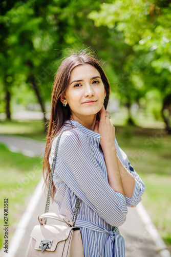A girl of Asian appearance on a walk in a city park. Summer portrait of young Tatar on a background of green foliage