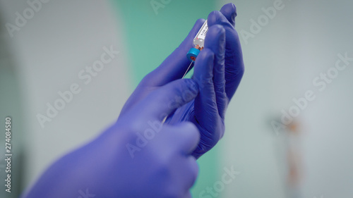 Hands in blue rubber gloves with syringe