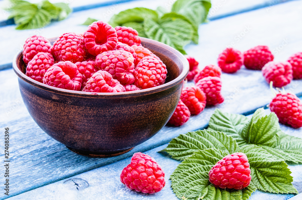Ripe red raspberries on a bowl against the background of blue boards. Selective focus. Ripe red raspberries on a bowl against the background of blue boards. Selective focus.