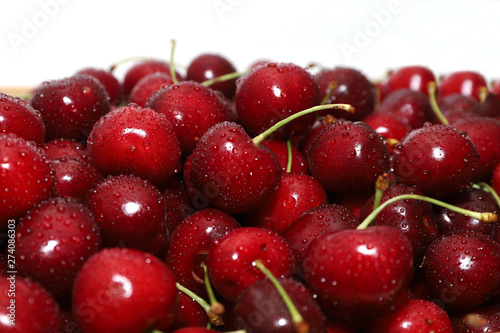 A bunch of ripe cherries with peduncles lies on a white background. Large collection of fresh red cherries. Ripe cherries background isolate