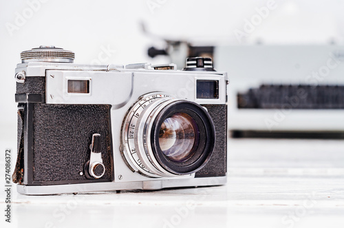 Old film camera on white plank background. Typewriter on the background. Vintage photo