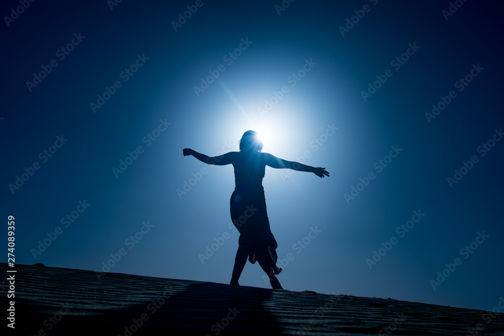 silhouette of young woman with long skirt dancing in evocative and confident way on top of desert dune at night