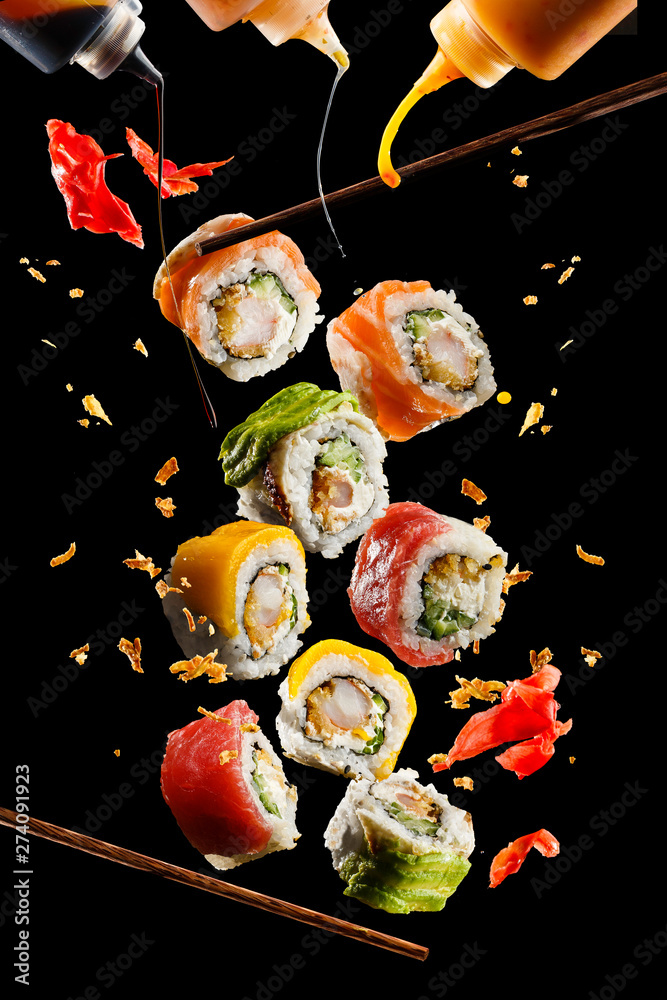 Flying pieces of sushi with wooden chopsticks and sauce, isolated on black background. Flying food and motion concept. Very high resolution image