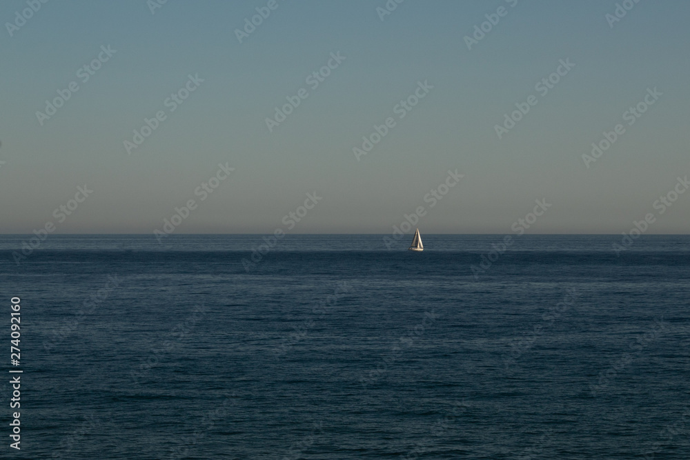 Sailing boat in the distance to the sea in the evening