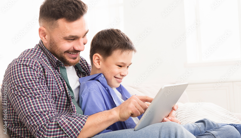 Young father teaching his son to use special application on digital tablet Young father teaching his son to use special application on digital tablet