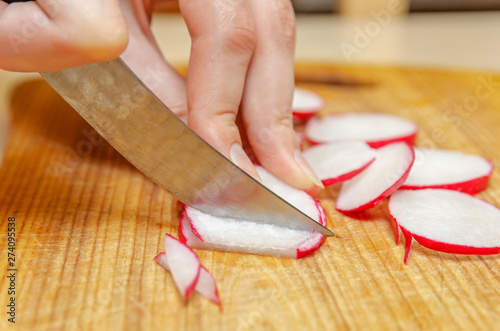 Female hands cut radish into small pieces on a wooden board close up