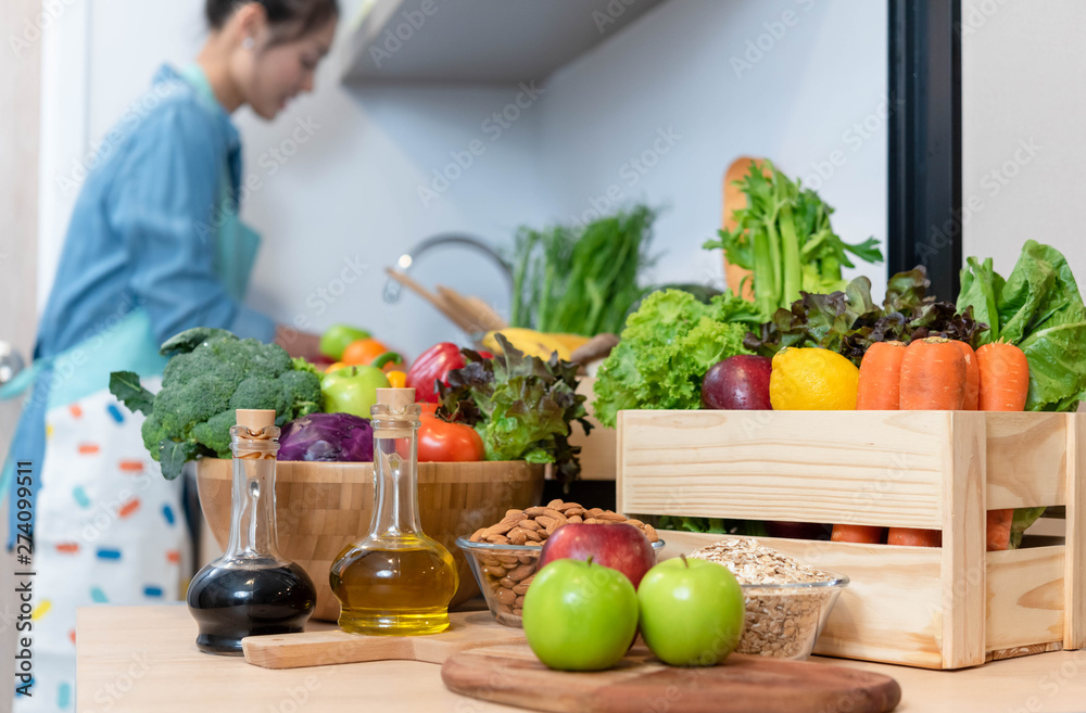 Pile of healthy food consist of vegetables, fruits and nuts with young woman washing fruits in background Pile of healthy food consist of vegetables, fruits and nuts with young woman washing fruits in background