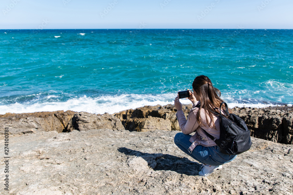 Woman crouching taking pictures of shore with smart phone