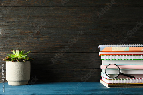 Composition with copybooks, succulent and magnifier on wood table against dark background
