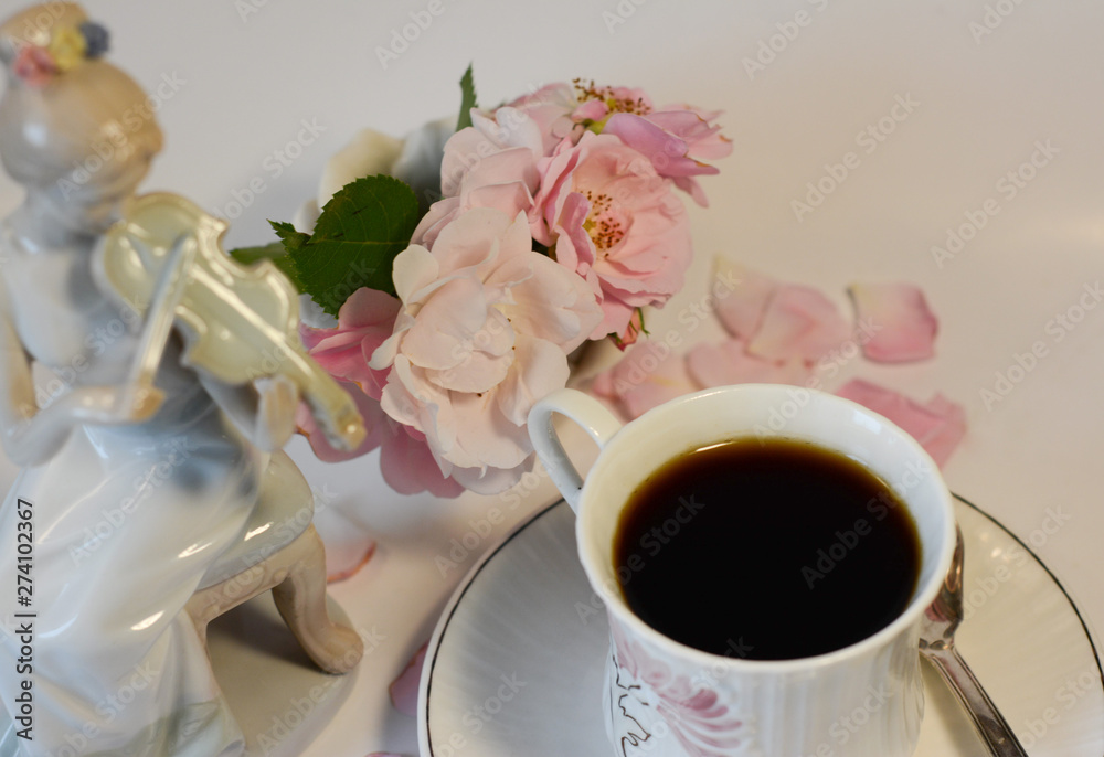 Beautiful tender still life in gently pink tones from a cup of coffee and a porcelain figurine of a girl playing the violin Beautiful tender still life in gently pink tones from a cup of coffee and a porcelain figurine of a girl playing the violin