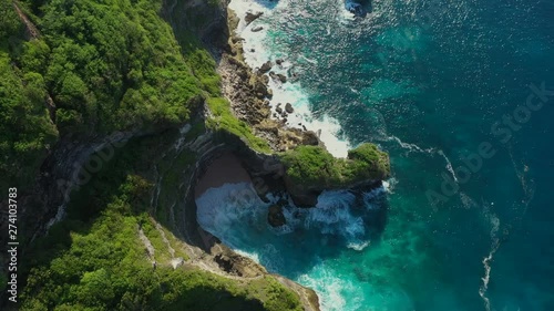 Bali - Bukit peninsula. Aerial footage of transparent turquoise ocean and rocky cliffs, covered with tropical trees.