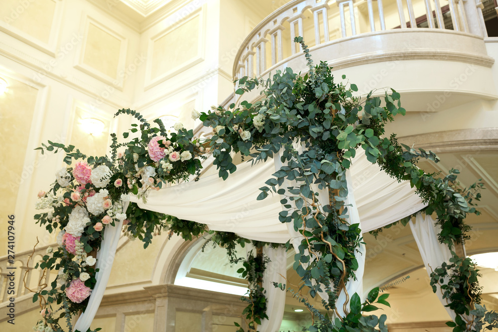 Wedding chuppah decorated with fresh flowers indoor banquet hall of wedding ceremony. Luxury wedding florist decoration artwork