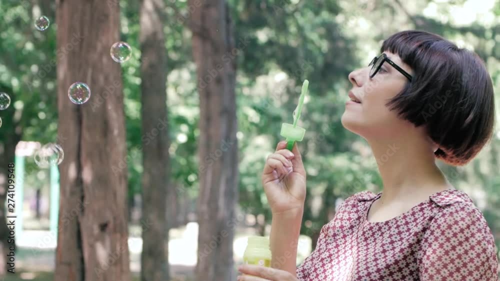 Young woman in glasses blowing bubbles outdoors in the park Young woman in glasses blowing bubbles outdoors in the park