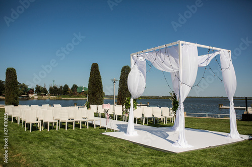 Beautiful outgoing wedding set up. Jewish Hupa  on romantic wedding ceremony , wedding outdoor on the lawn water view. Wedding decor. White wooden chairs on a green lawn. White armchairs for guests photo