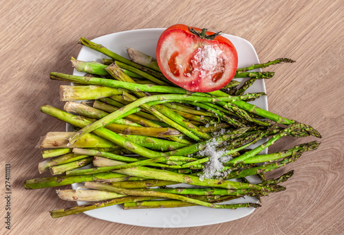 View from above of a bundle of cooked green asparagus and a red tomato, with a handful of salt on top photo