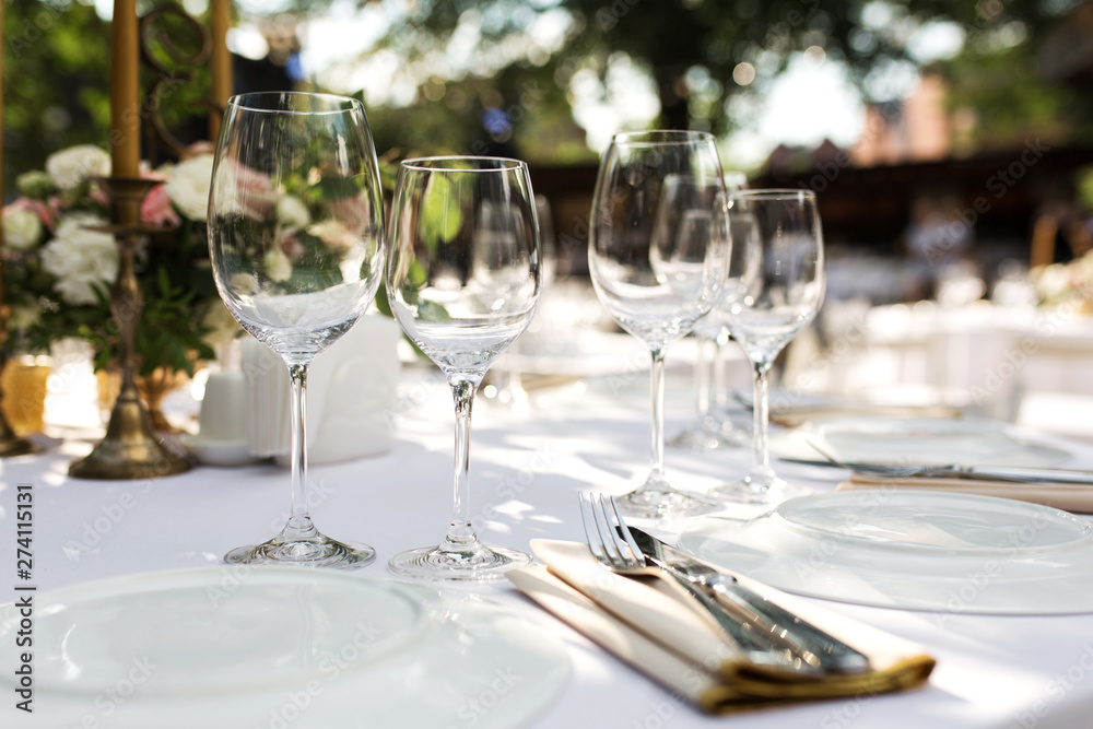 Wedding table setting decorated with fresh flowers in a brass vase. Wedding floristry. Banquet table for guests outdoors with a view of green nature. Bouquet with roses, eustoma and eucalyptus leaves