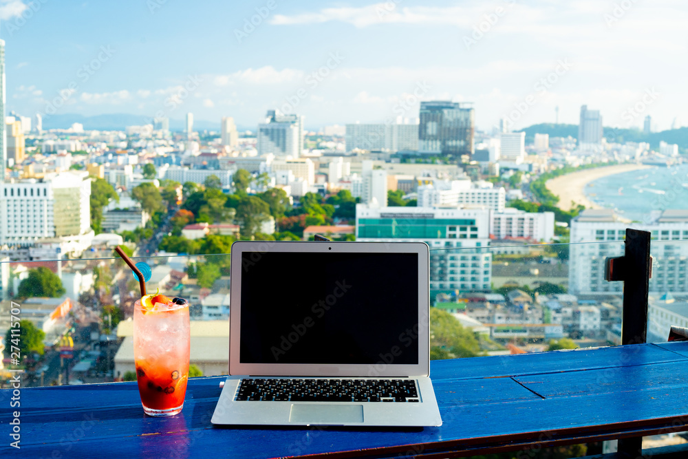 Laptop and glass of summer cocktail on wooden table, on bright beautiful panoramic background of Pattaya city, Thailand. Laptop and glass of summer cocktail on wooden table, on bright beautiful panoramic background of Pattaya city, Thailand.