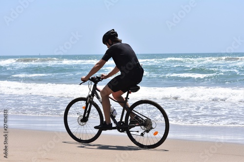 Cyclist riding in the edge of water on a deserted beach