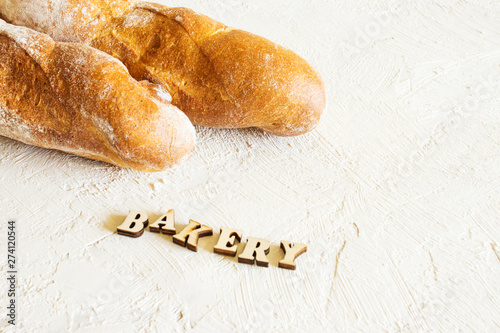 Baguette on a light background. The inscription "bakery" in wooden letters on a textural background. Place for text.