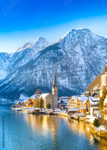 Classic postcard view of famous Hallstatt lakeside town in the Alps with traditional passenger ship on a beautiful cold sunny day with blue sky and clouds in winter, Salzkammergut region, Austria
