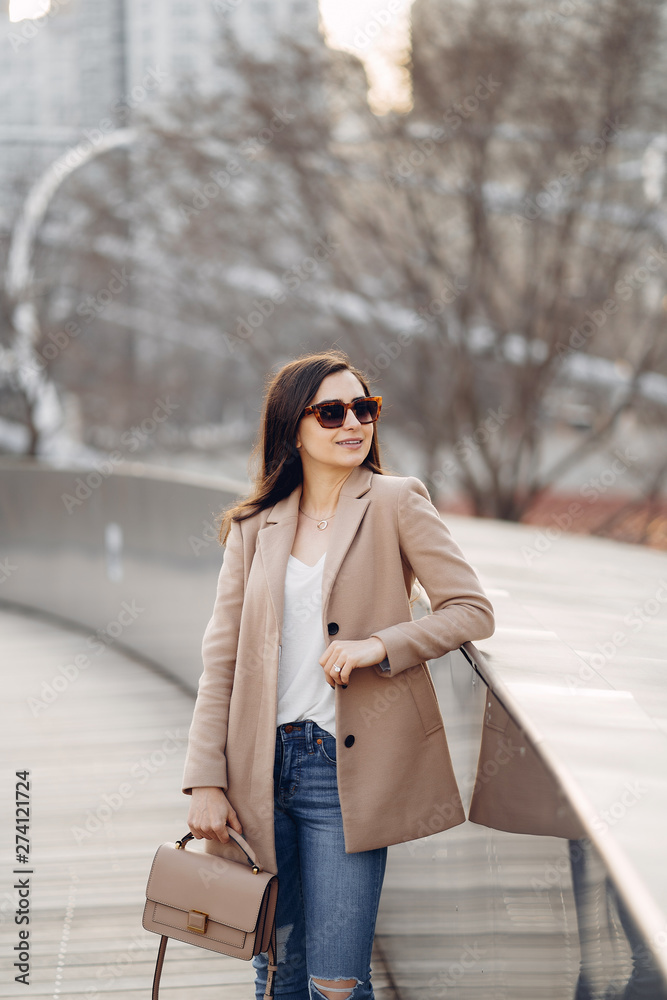 Fototapeta premium Beautiful girl in a park. Stylish brunette in a brown jacket. Lady in a sunglasses