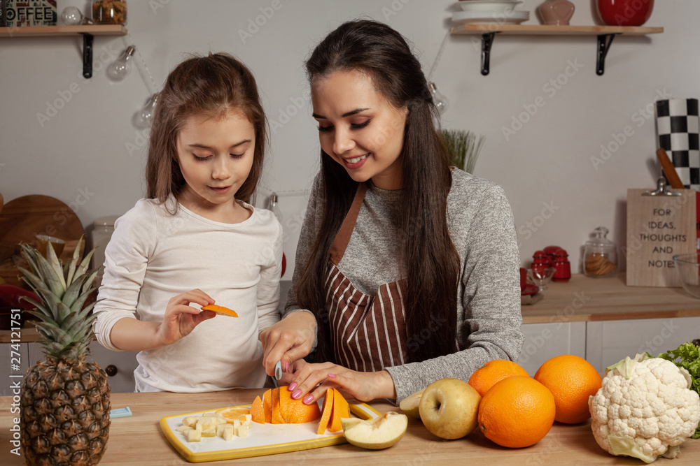 Mother and her daughter are doing a fruit cutting and having fun at the kitchen. Mother and her daughter are doing a fruit cutting and having fun at the kitchen.