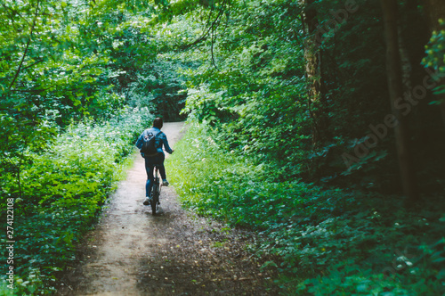 Woman biker riding a bicycle on the road through the woods. back view of young woman stands up to pedal along a steep climb