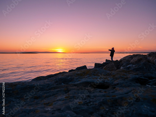 Silhouette of teenager girl pointing at sun set over ocean, Galway bay, Ireland. Concept, childhood, adventure, excitement.