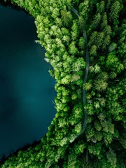 Aerial top view of country road in green summer forest and blue lake. Rural landscape in Finland.
