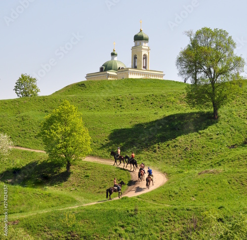 Green hilly terrain in spring. Horsemen are riding along a country road.