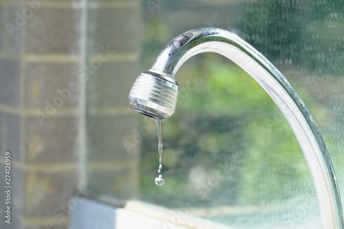 In selective focus water flowing from a steel faucet in a public restroom for saving water concept 