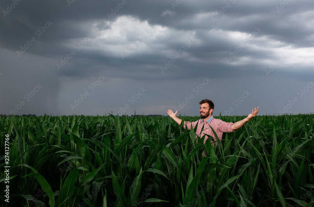 Portrait of young farmer standing in corn field with his hands outstretched.