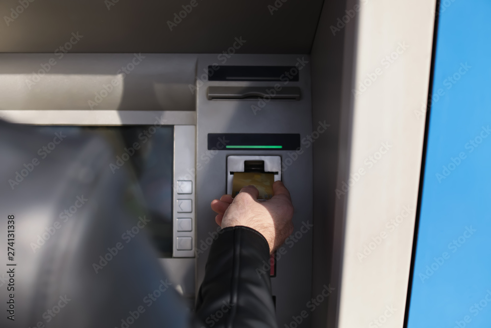 Man inserting credit card into cash machine outdoors, closeup Man inserting credit card into cash machine outdoors, closeup