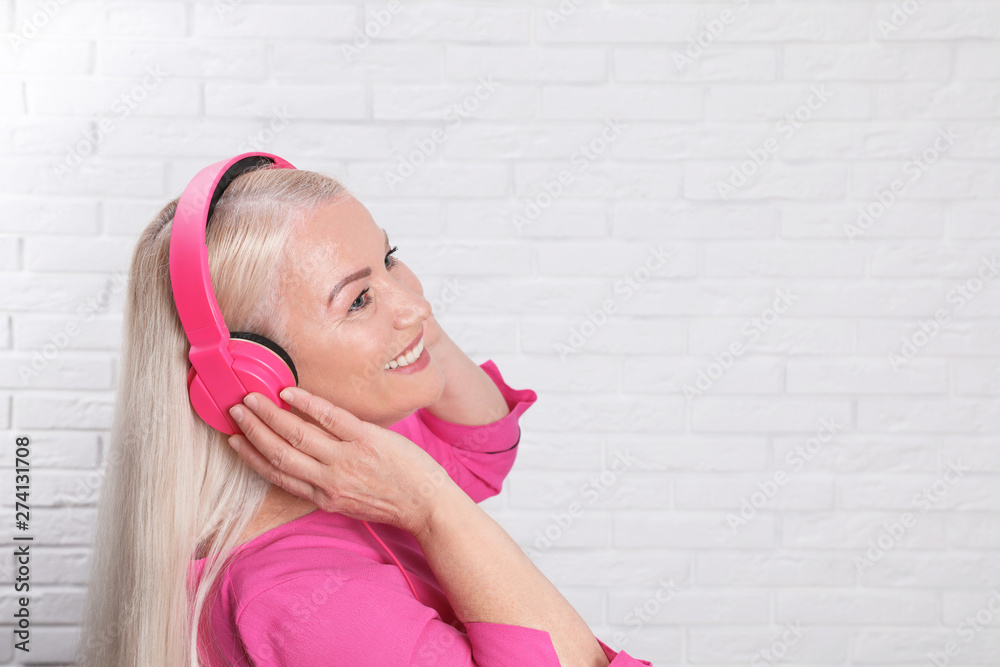 Mature woman enjoying music in headphones against brick wall. Space for text Mature woman enjoying music in headphones against brick wall. Space for text