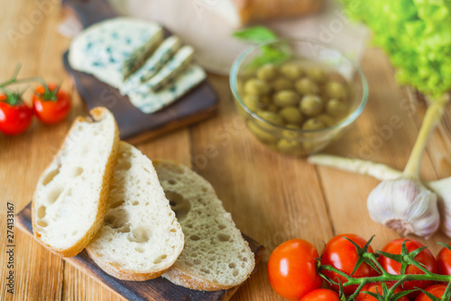 Ingredients for cooking bruschetta: chopped ciabatta, olives, tomatoes, blue cheese on a wooden background. Cooking healthy and tasty food.