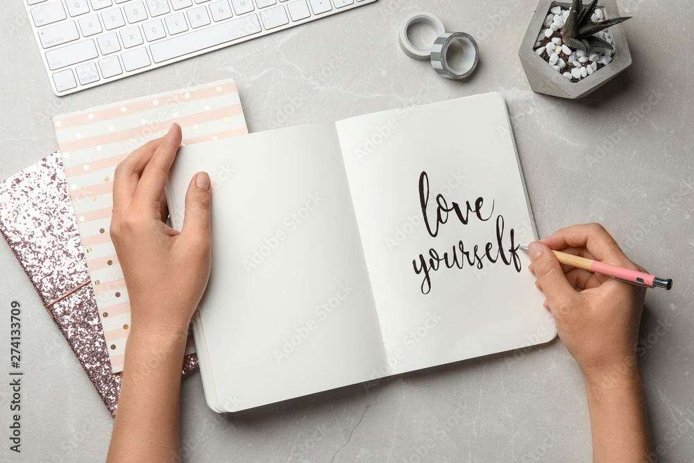 Woman writing LOVE YOURSELF in journal on grey table, flat lay - obrazy, fototapety, plakaty 