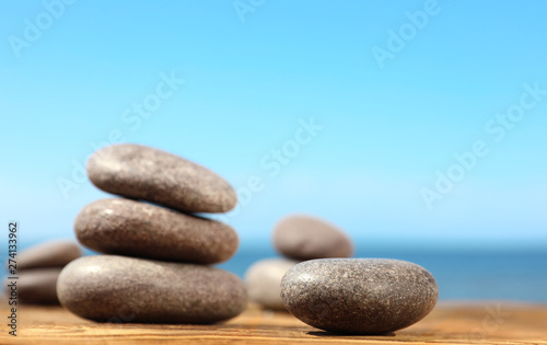 Stones on wooden table against seascape, space for text. Zen concept