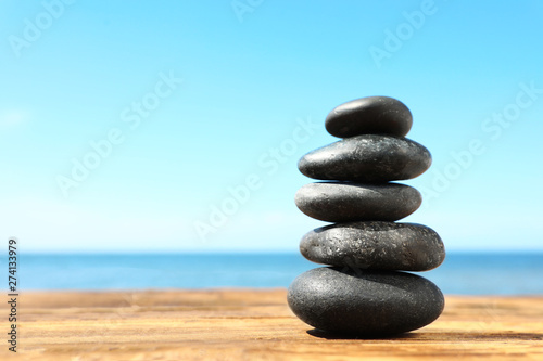 Stack of stones on wooden table against seascape  space for text. Zen concept