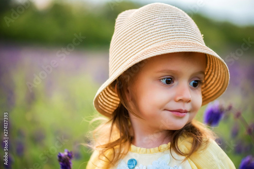 Cute baby in hat girl looks aside outdoors in green field. Child portrait