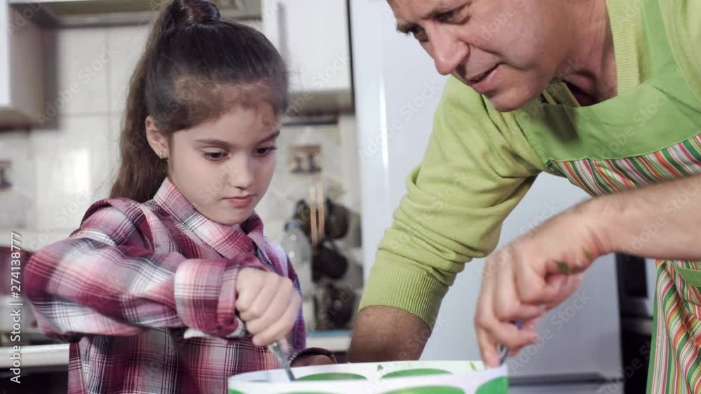 little girl with brown hair mixes actively products in big green bowl using spoon under guidance of father wearing apron little girl with brown hair mixes actively products in big green bowl using spoon under guidance of father wearing apron