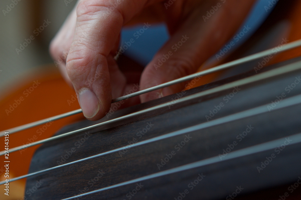 Caucasian womans hand plucking cello strings close up Caucasian womans hand plucking cello strings close up