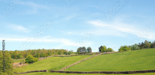 panoramic view of sunlit summer countryside with green rolling hilly meadows surrounded by stone walls and forest trees above hardcastle crags in calderdale