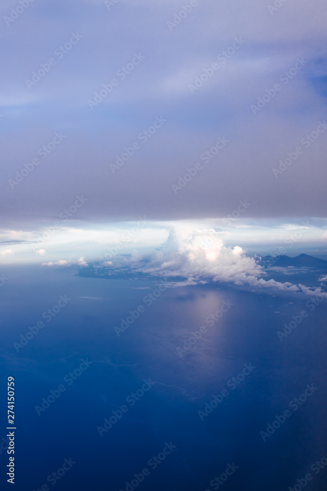 Plane window view with blue sky and clouds. Clouds and sky as seen through window of an aircraft. View of beautiful cloud, ocean and city from the airplane.